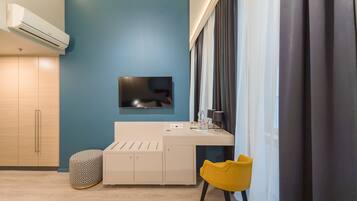 Habitació moderna amb una paret d'accent blava, un televisor de pantalla plana fixat sobre un escriptori blanc, una cadira groga i un otomà estampat.