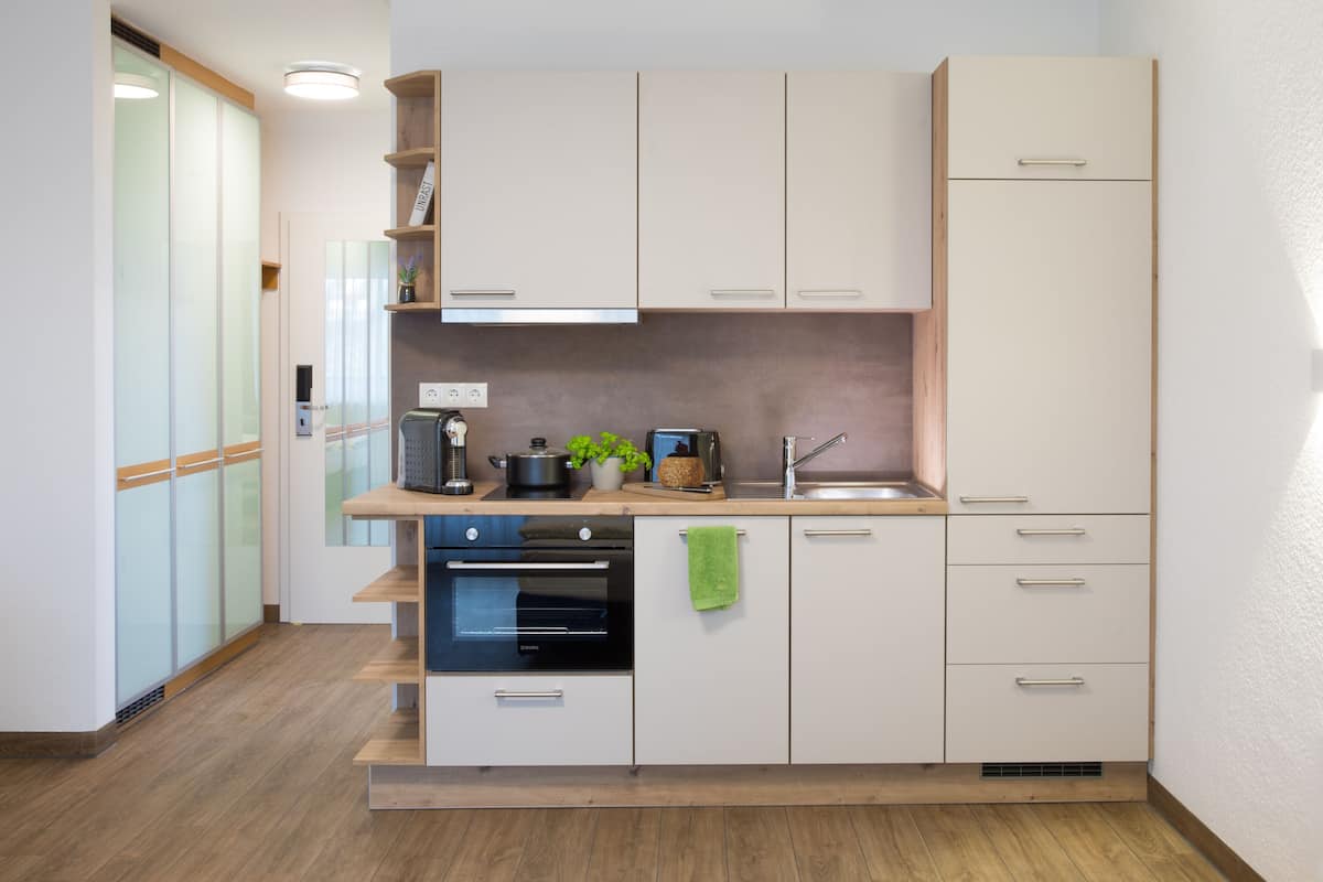 A modern kitchen with white cabinets, a built-in oven, a sink, and a countertop with a plant and a kettle.