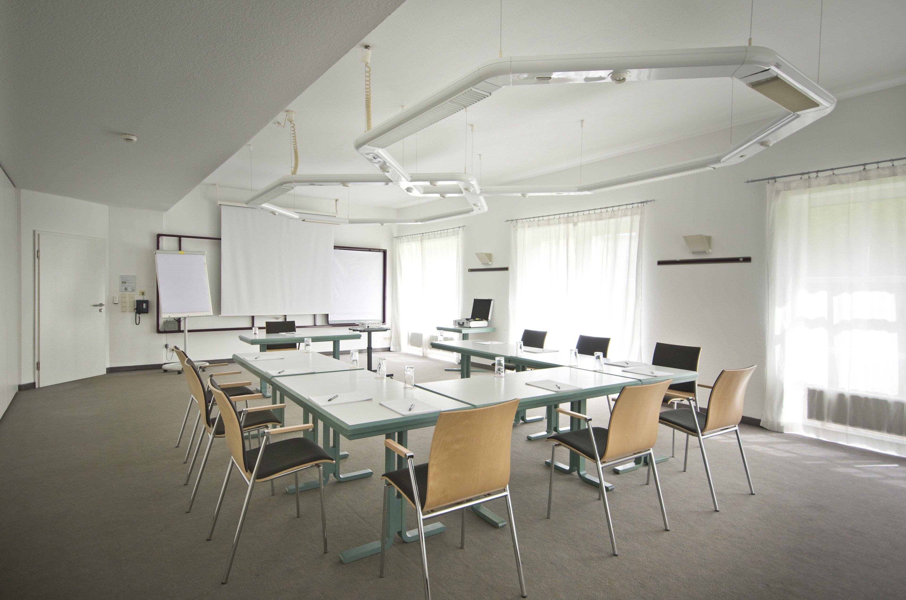 A conference room with a long table, chairs, a whiteboard, and a projector screen.