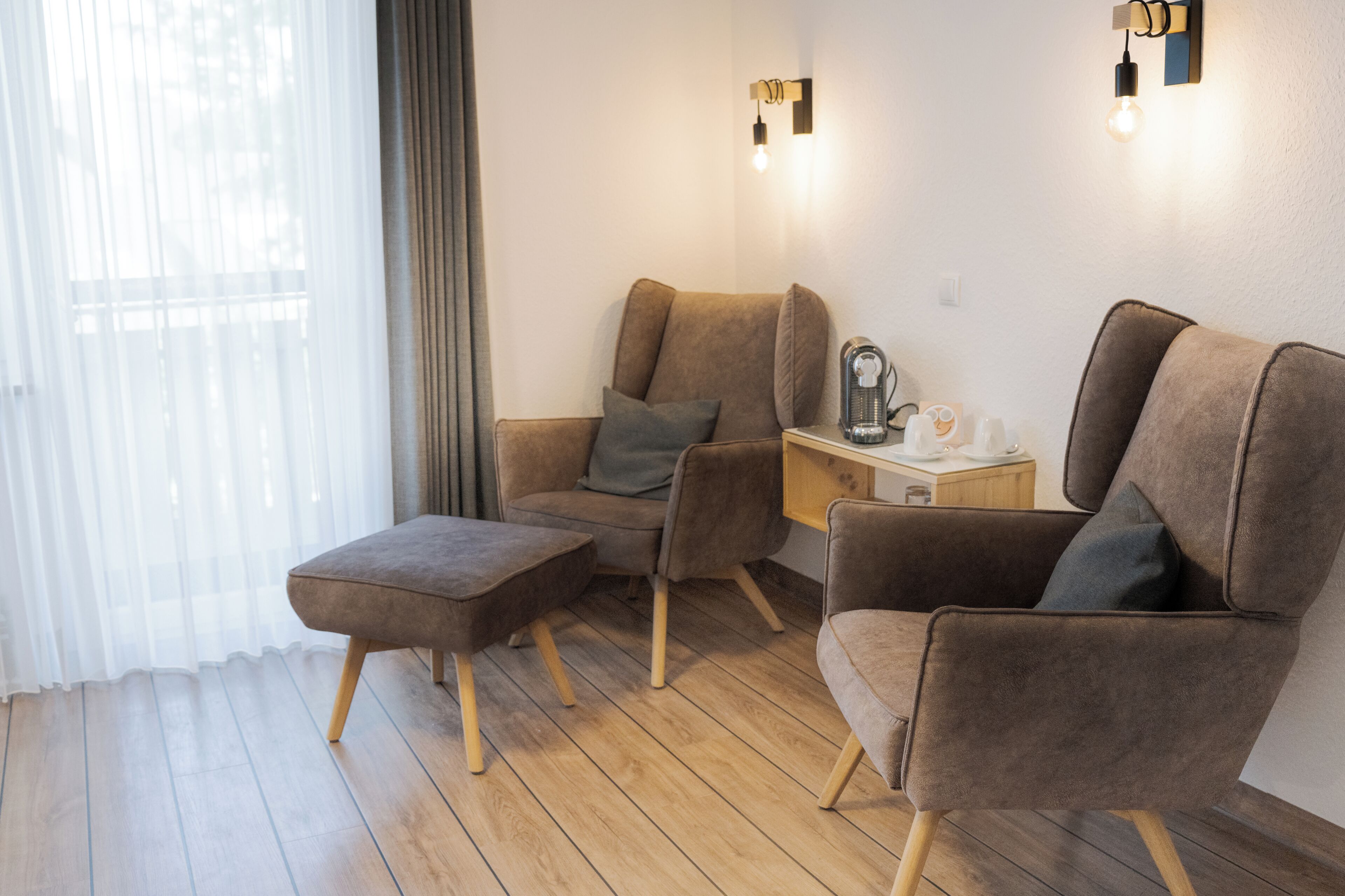 Una sala de estar moderna con un sofá, sillón, reposapiés y una mesita con lámpara.