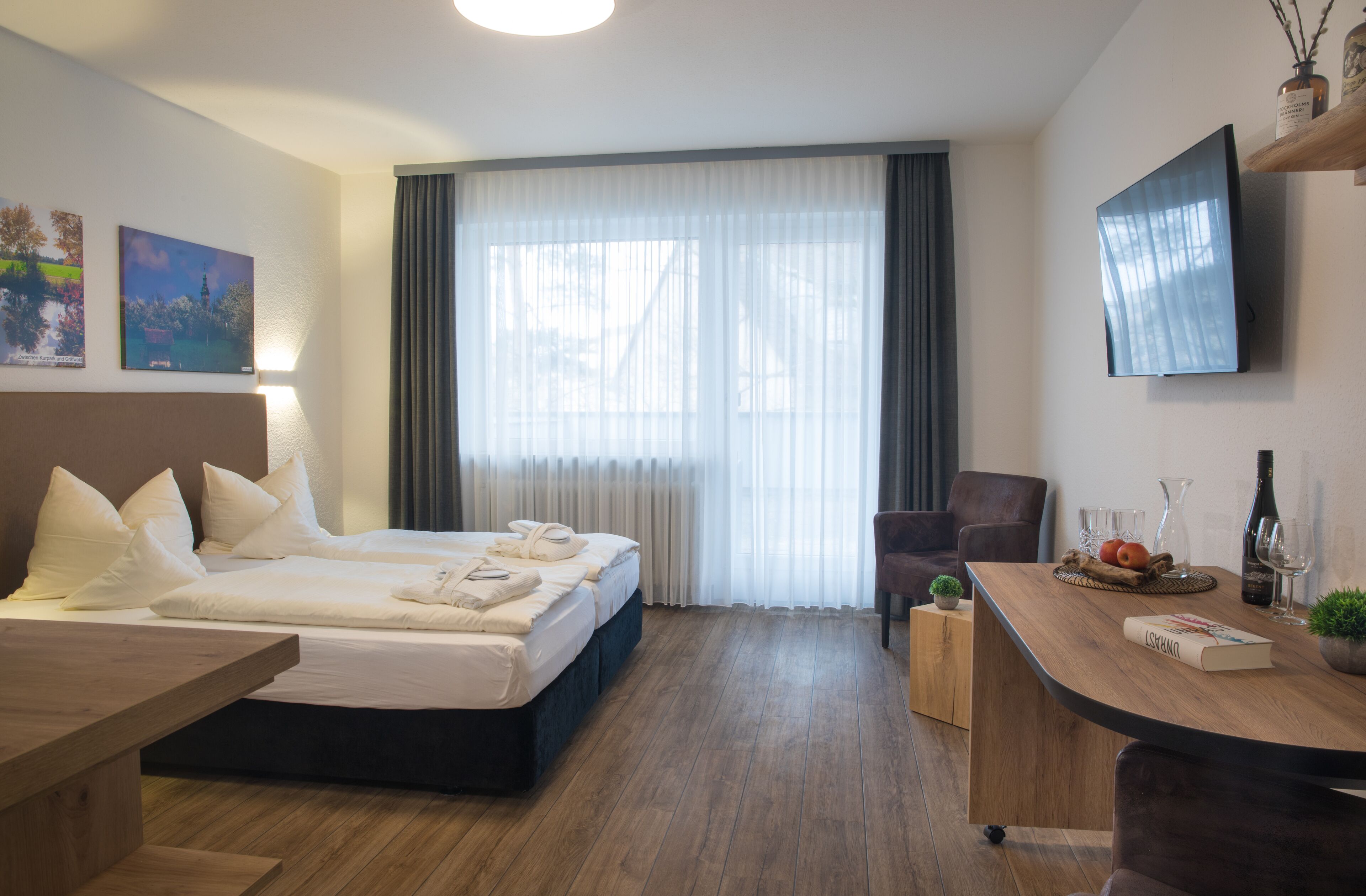 Habitación de hotel con cama, escritorio, silla, televisor y ventana con cortinas.