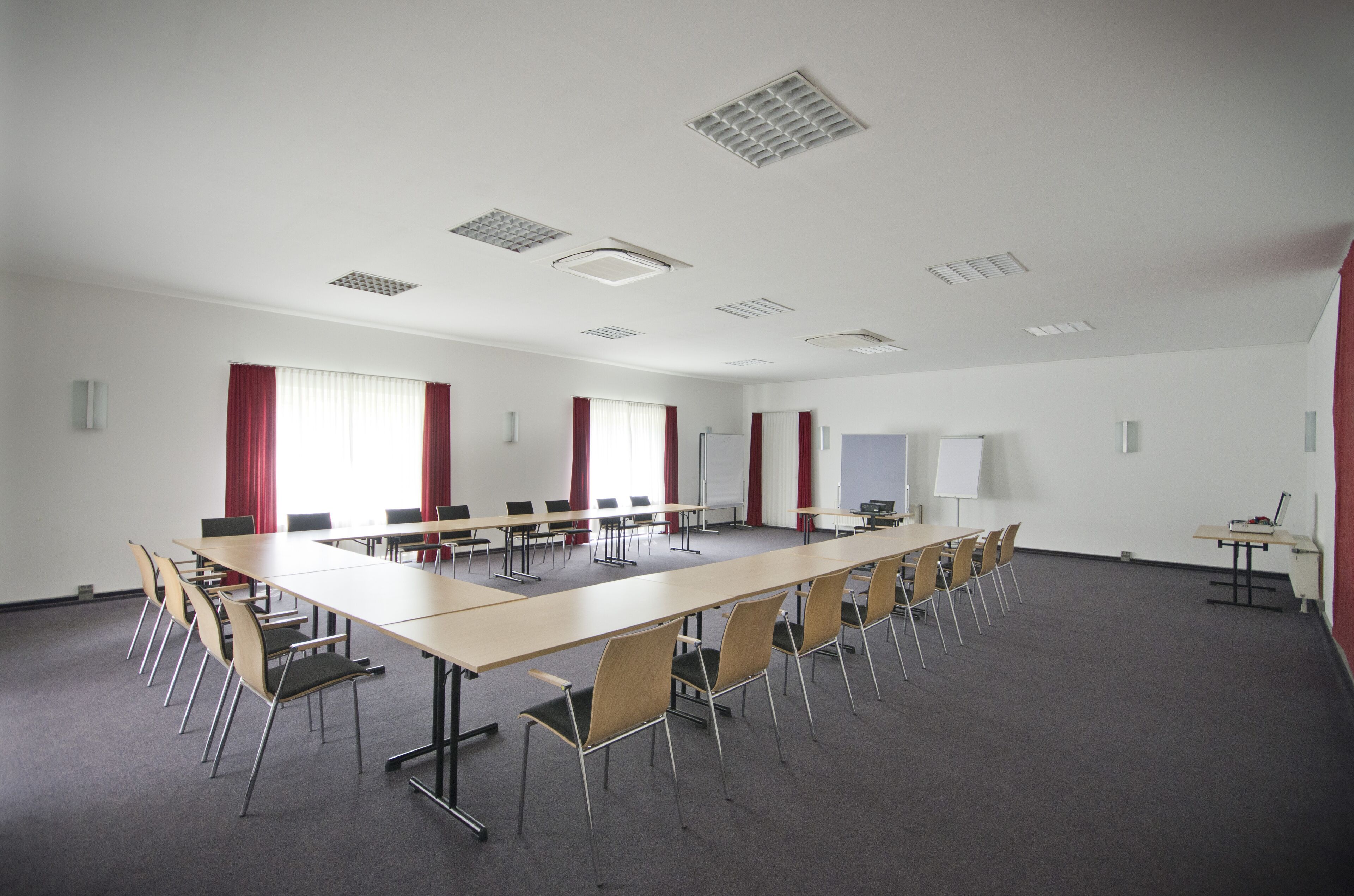 A conference room with a long table, multiple chairs, whiteboard, and red curtains.