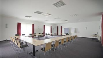 A conference room with a long table, multiple chairs, whiteboard, and red curtains.