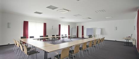 A conference room with a long table, multiple chairs, whiteboard, and red curtains.