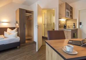 Una habitación de hotel con una cama, un escritorio con una computadora portátil, una taza y una zona de ducha.