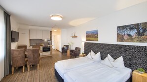 A hotel room with a large bed, a desk, and a chair. There is a television on the wall and a window with a view of a house. - Hotel Am Kurpark Späth (Bad Windsheim)