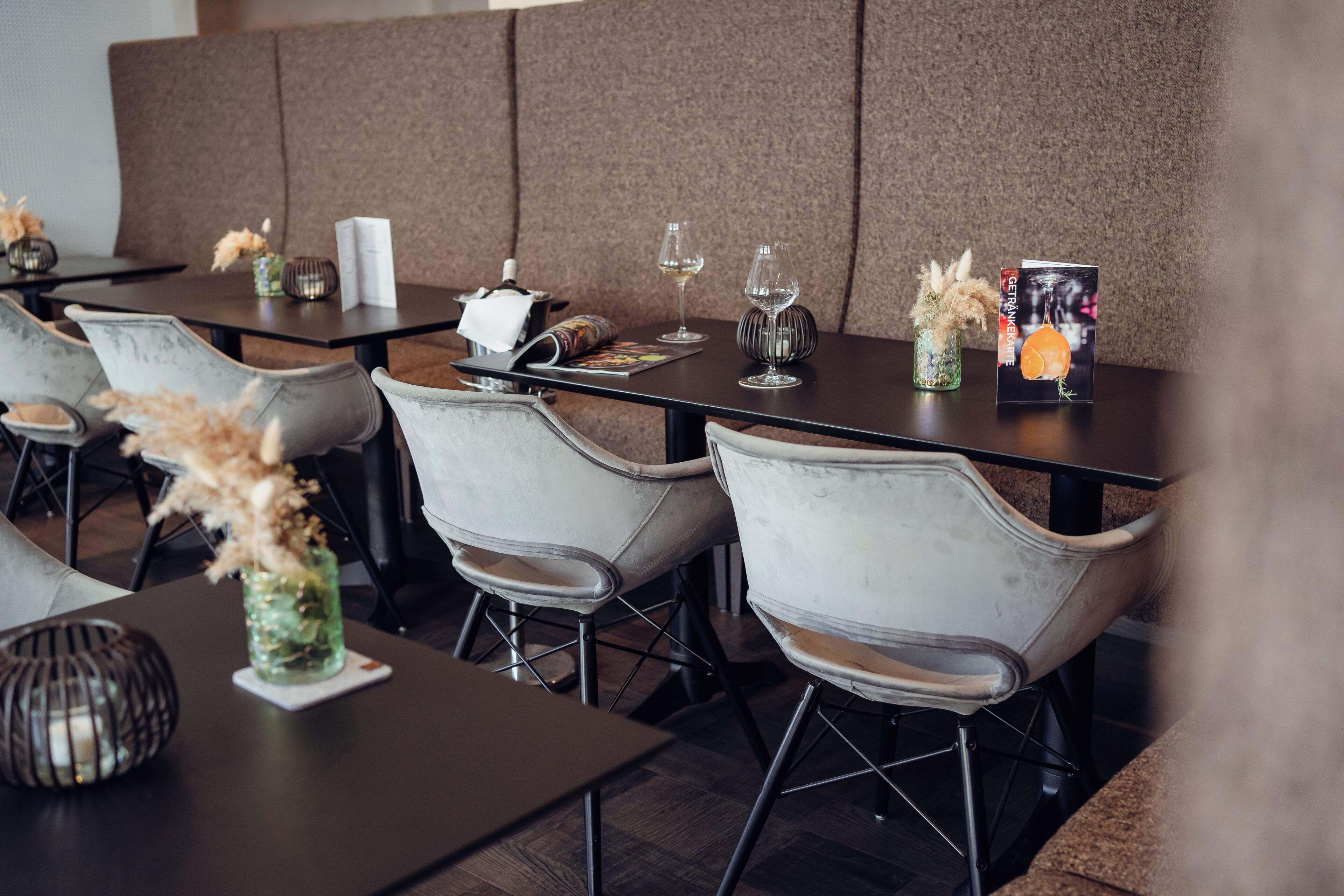 Interior de restaurante con mesas, sillas y diferentes tipos de mesas dispuestas, incluyendo copas de vino y menús.