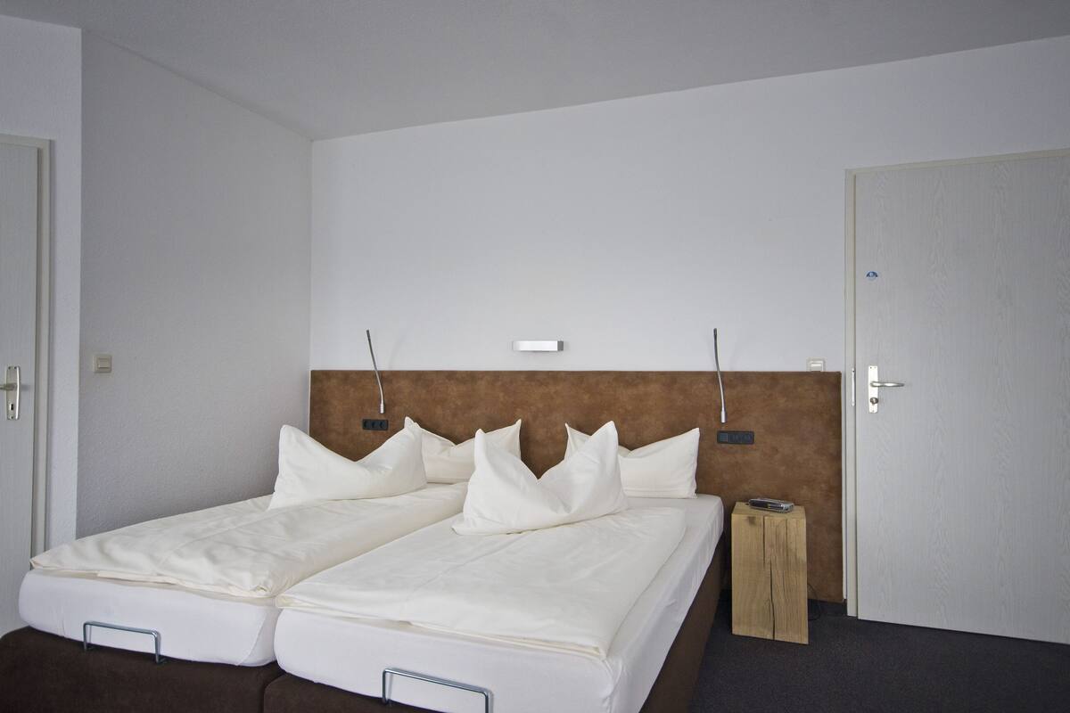A double bed with white linens and a headboard, a bedside table, and a door with a handle.