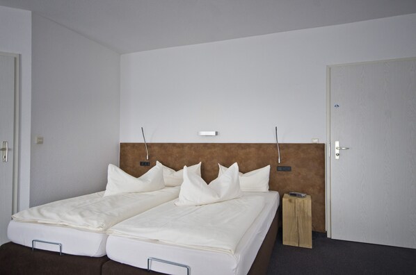 A double bed with white linens and a headboard, a bedside table, and a door with a handle.