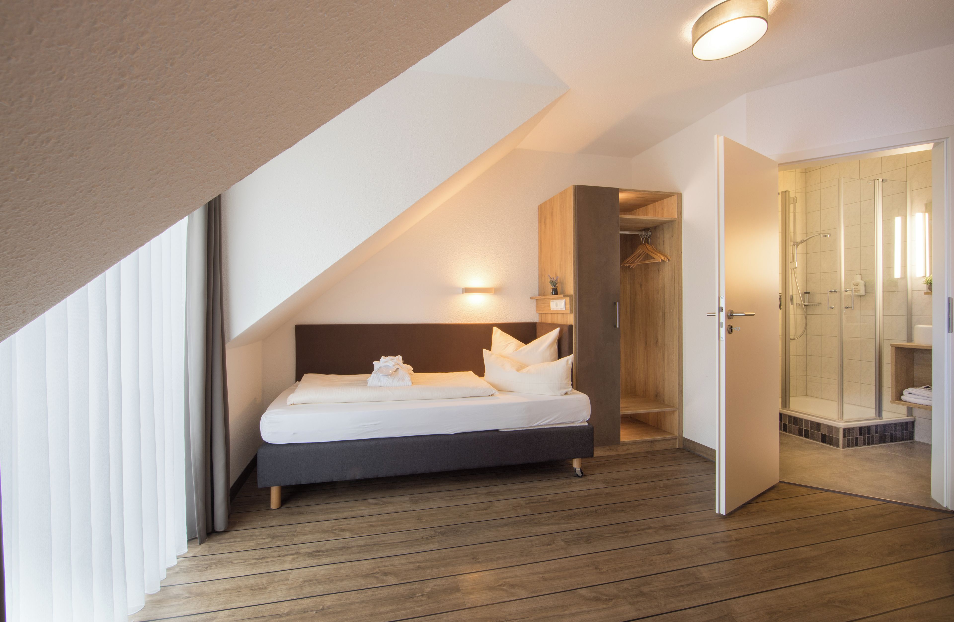 A modern bedroom with a bed, a wooden wardrobe, and a shower area.