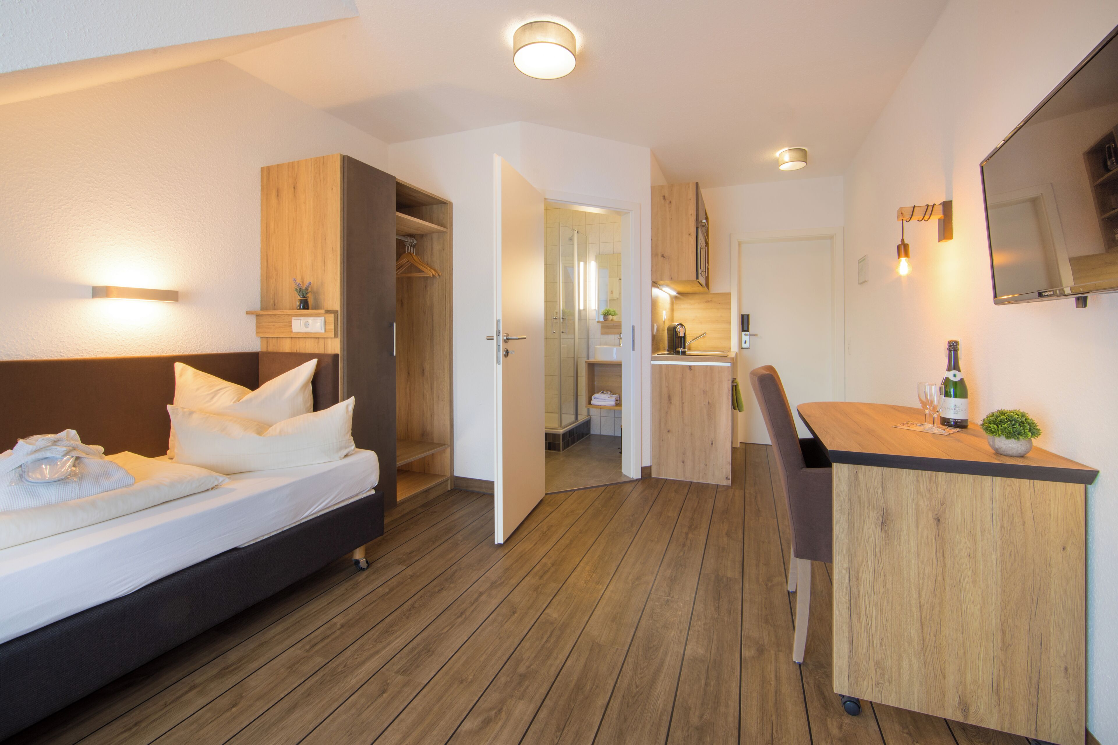 A modern hotel room with a bed, a desk, and a kitchenette.