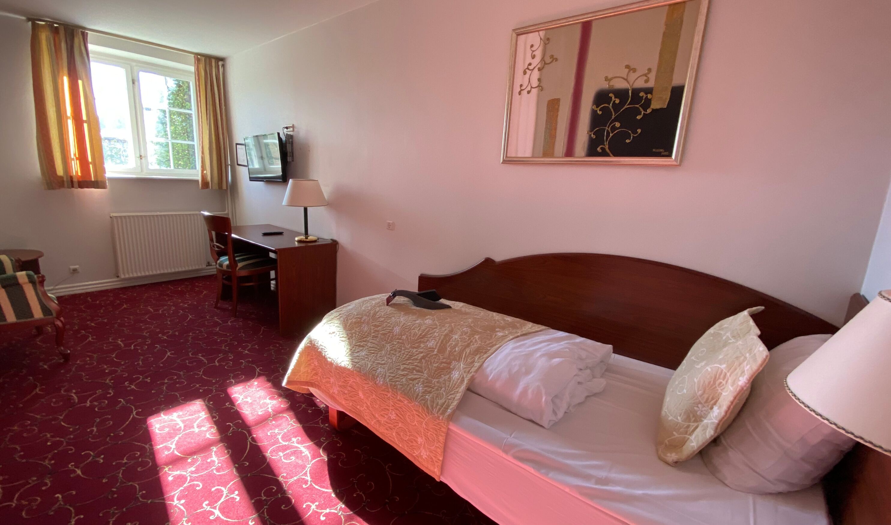 A hotel room with a large bed, a desk with a chair, a television, and a window with curtains.