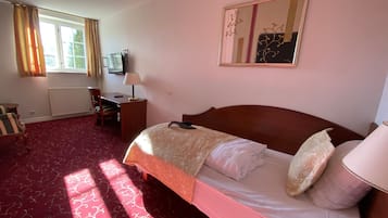 Ein Hotelzimmer mit einem großen Bett, einem Schreibtisch mit Stuhl, einem Fernseher und einem Fenster mit Vorhängen.