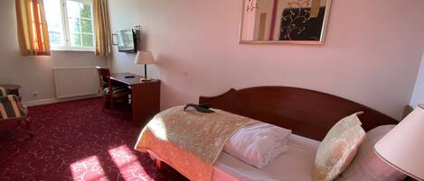 A hotel room with a large bed, a desk with a chair, a television, and a window with curtains.