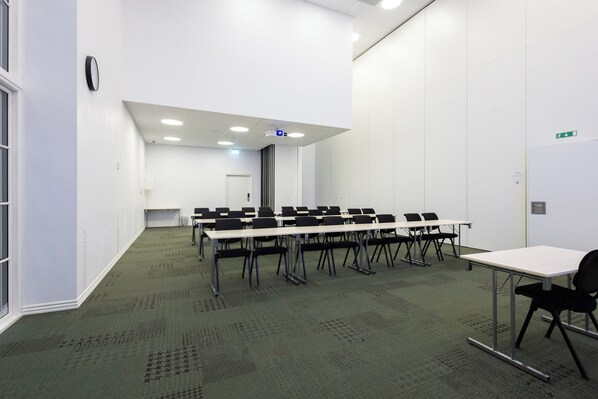 Une salle de conférence dotée de plusieurs tables et chaises, de murs blancs et d’un sol recouvert de moquette.