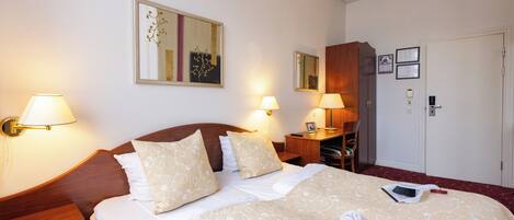 Una habitación de hotel con una cama bien hecha, dos lámparas de noche, un cabecero de madera, un escritorio con una silla y una puerta con manija.