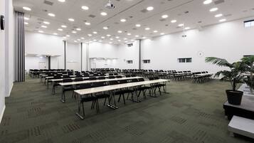 A large conference room with rows of tables and chairs, a projector, and a clock on the wall.