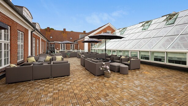 A rooftop terrace with a brick floor, multiple sofas, and umbrellas. - Milling Hotel Park (Middelfart)