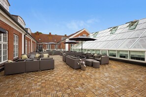 A rooftop terrace with a brick floor, multiple sofas, and umbrellas. - Milling Hotel Park (Middelfart)
