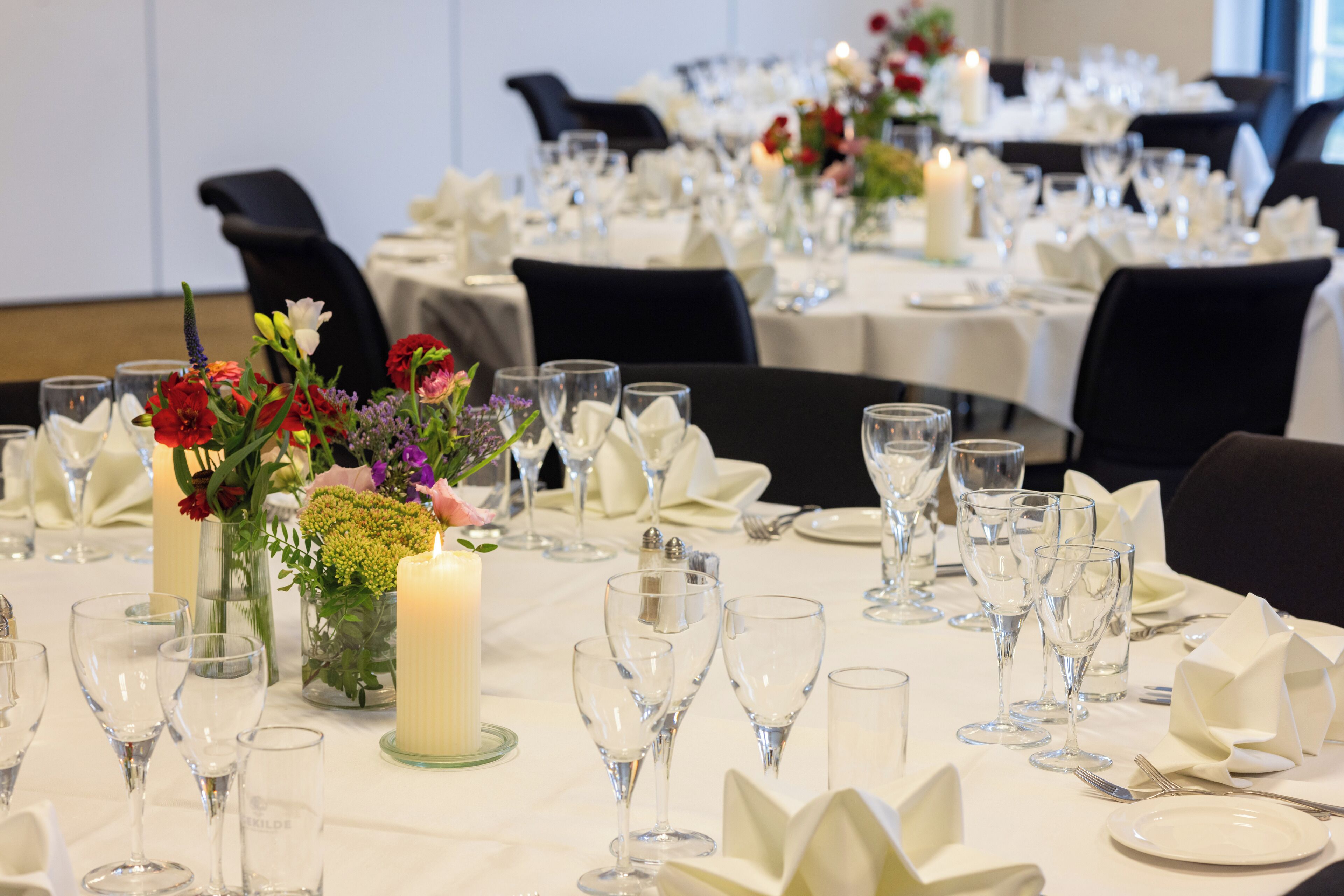 Un salón de banquetes con mesas dispuestas para un evento formal, con centros de mesa florales y velas.