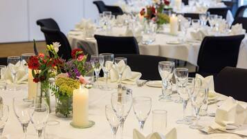 Une salle de banquet où les tables sont dressées pour un événement formel, agrémentées de compositions florales et illuminées par des bougies.