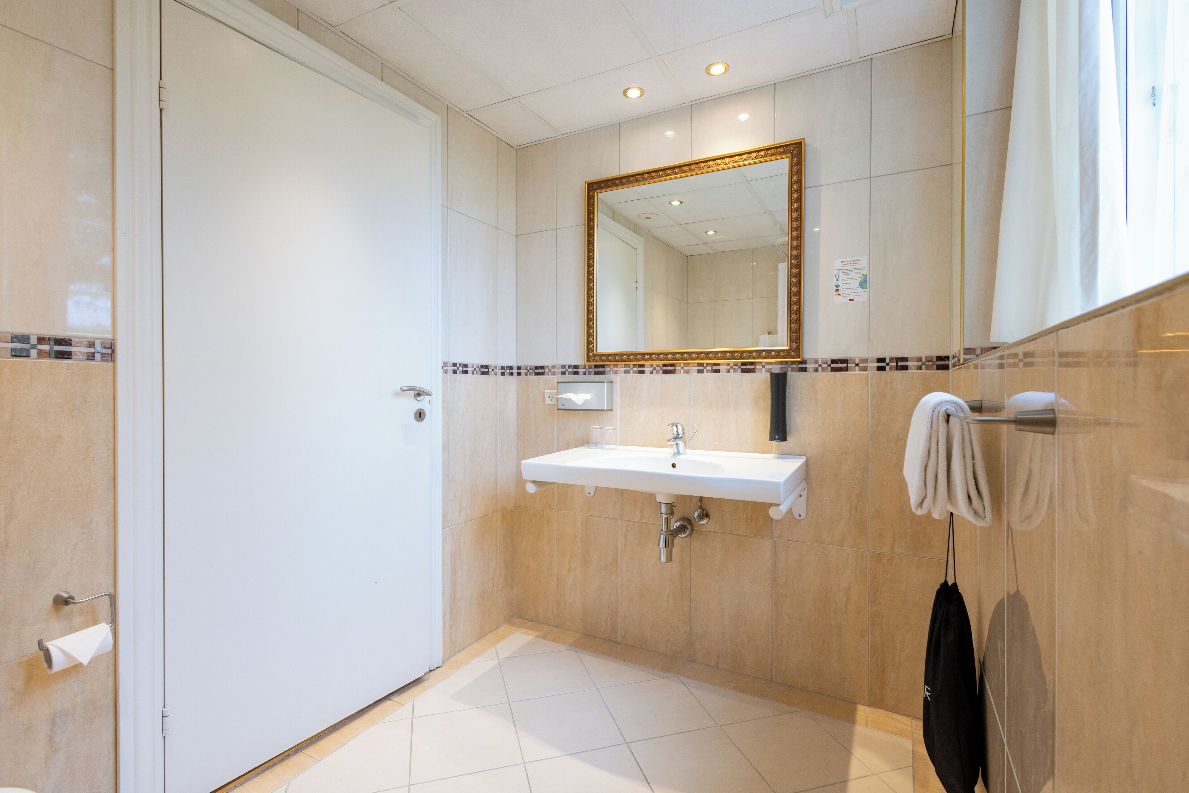 Un baño moderno con un lavamanos blanco, un espejo grande y un perchero para toallas.
