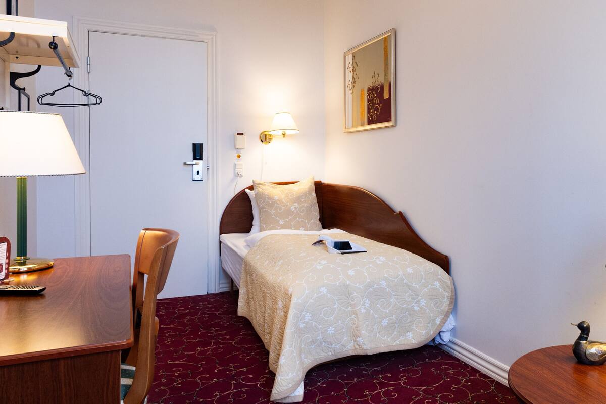 Ein Hotelzimmer mit einem Bett, einem Schreibtisch, einem Stuhl, einer Lampe und einem an der Wand hängenden Bild.