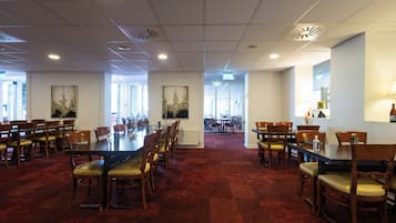 A spacious conference room with multiple tables and chairs, large windows, and ceiling vents.