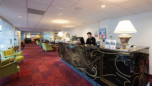 A hotel reception area with a reception desk, a receptionist, and a red carpeted floor. - Milling Hotel Park (Middelfart)