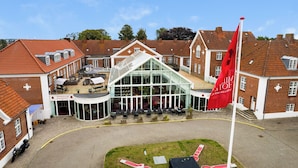 A traditional brick building with a glass conservatory, outdoor seating, and a red flag. - Milling Hotel Park (Middelfart)