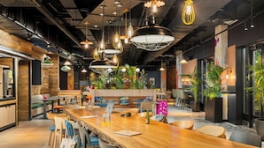 Un café moderne avec un long comptoir en bois, plusieurs espaces pour s’asseoir et des lampes suspendues.