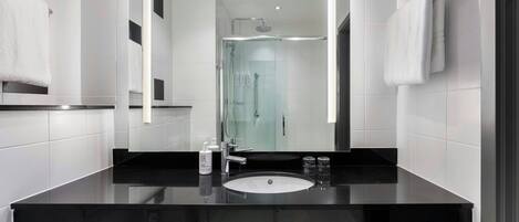 A modern bathroom with a black countertop, white sink, and a glass-enclosed shower.