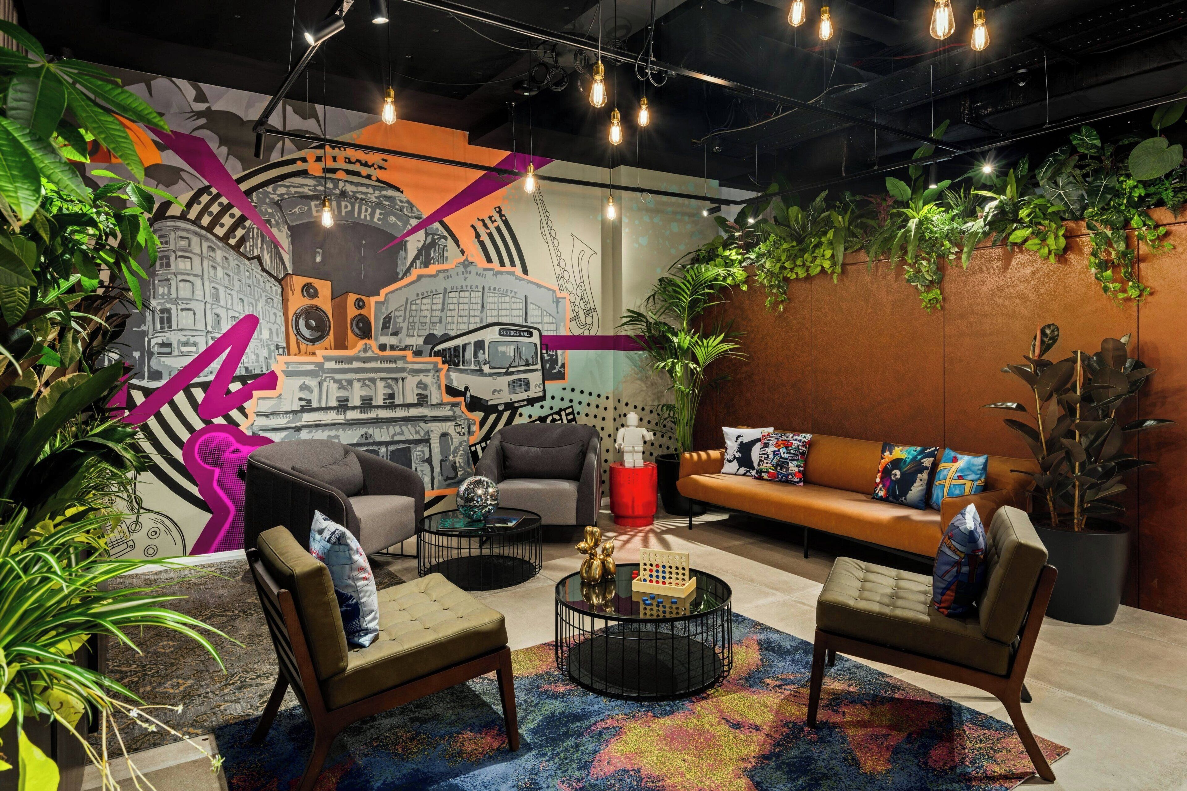 A modern lounge area with a mural, comfortable seating, and abundant greenery.
