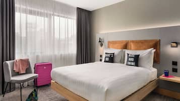 A modern hotel room with a large bed, a chair, a suitcase, and a nightstand.