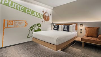 Ett modernt hotellrum med en stor säng, en liten soffa och en vägg med en skylt som visar texten ”PURE CLASS” samt en karta över Belfast.