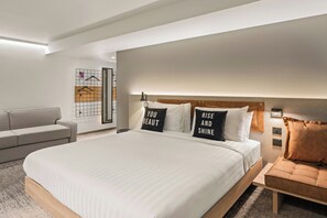 Une chambre d’hôtel moderne avec un grand lit, un canapé et un porte-manteaux fixé au mur.