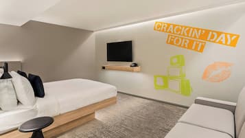 A modern hotel room with a bed, a sofa, a small table, and a TV mounted on the wall.
