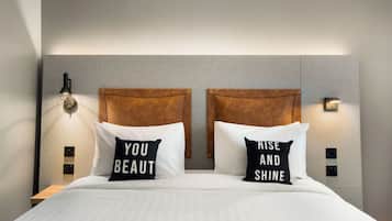 A neatly made bed with two pillows, one with "YOU BEAUTY" and the other with "RISE AND SHINE".