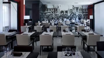 Un restaurant avec de nombreuses tables et chaises, une grande fresque murale et une vue sur une rue animée.