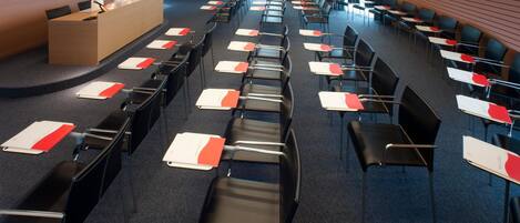 Un salón de conferencias con filas de sillas y mesas, un atril y un cartel.