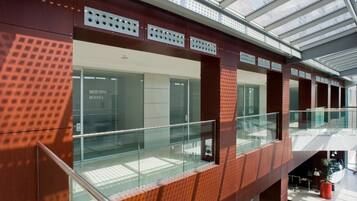 Un edificio moderno con fachada de vidrio, un entrepiso con barandilla de vidrio y un cartel que indica 'Meeting Room 1'.