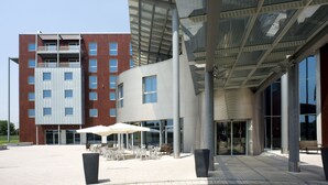 A modern building with a glass entrance and outdoor seating area. - Domina Milano Fiera (Novate Milanese)