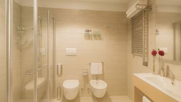A modern bathroom with a glass shower enclosure, two toilets, a sink, and a mirror.