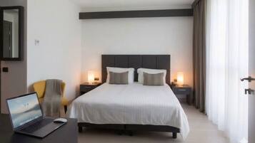 A hotel room with a bed, bedside lamps, a laptop on a desk, and a chair.
