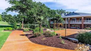 A building with a brick facade, a covered patio area, and a landscaped garden with a pathway. - The Lodge at Kiln Creek Resort (Newport News)