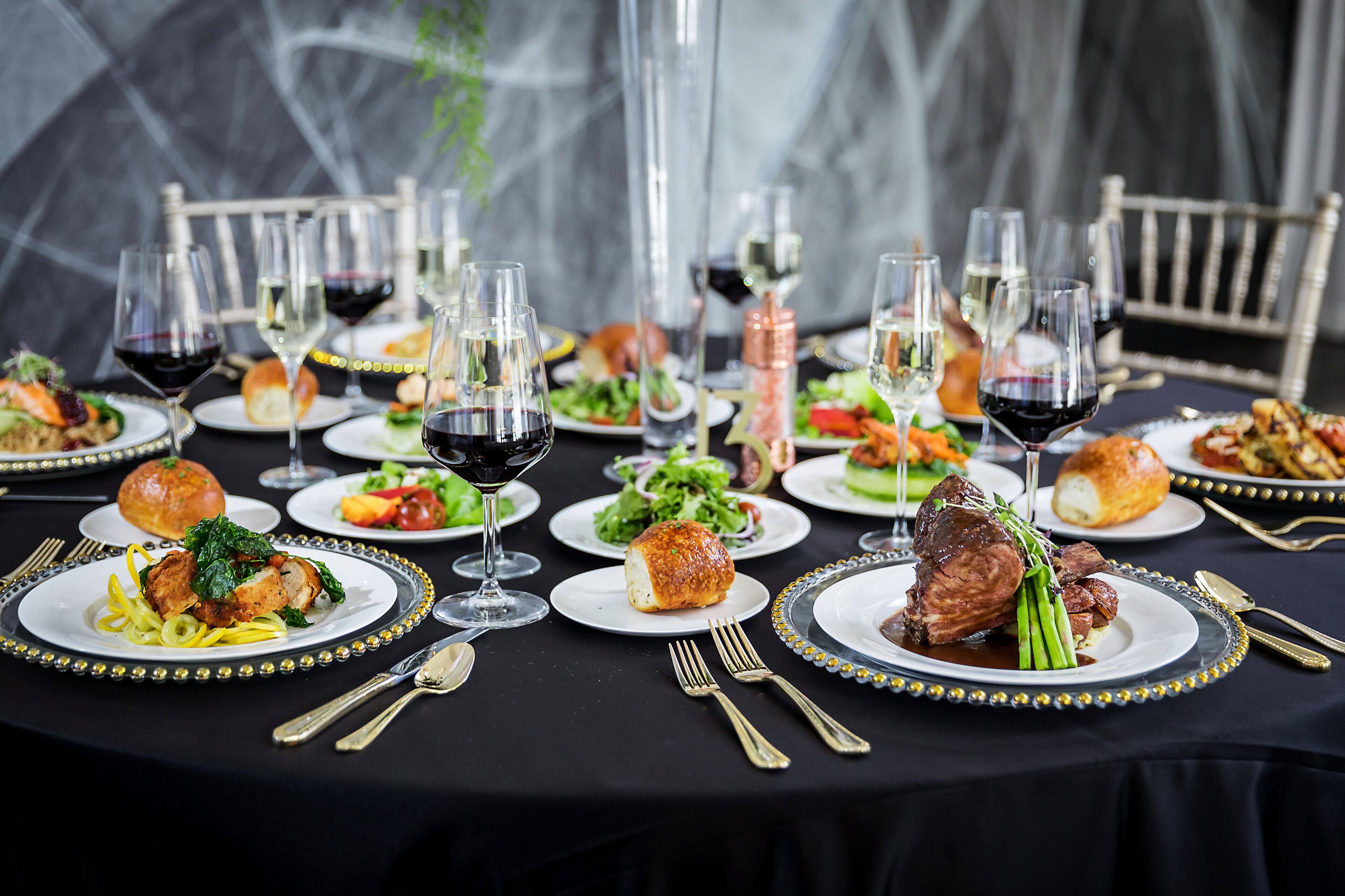 A formal dining table set with multiple plates of food, wine glasses, and cutlery.
