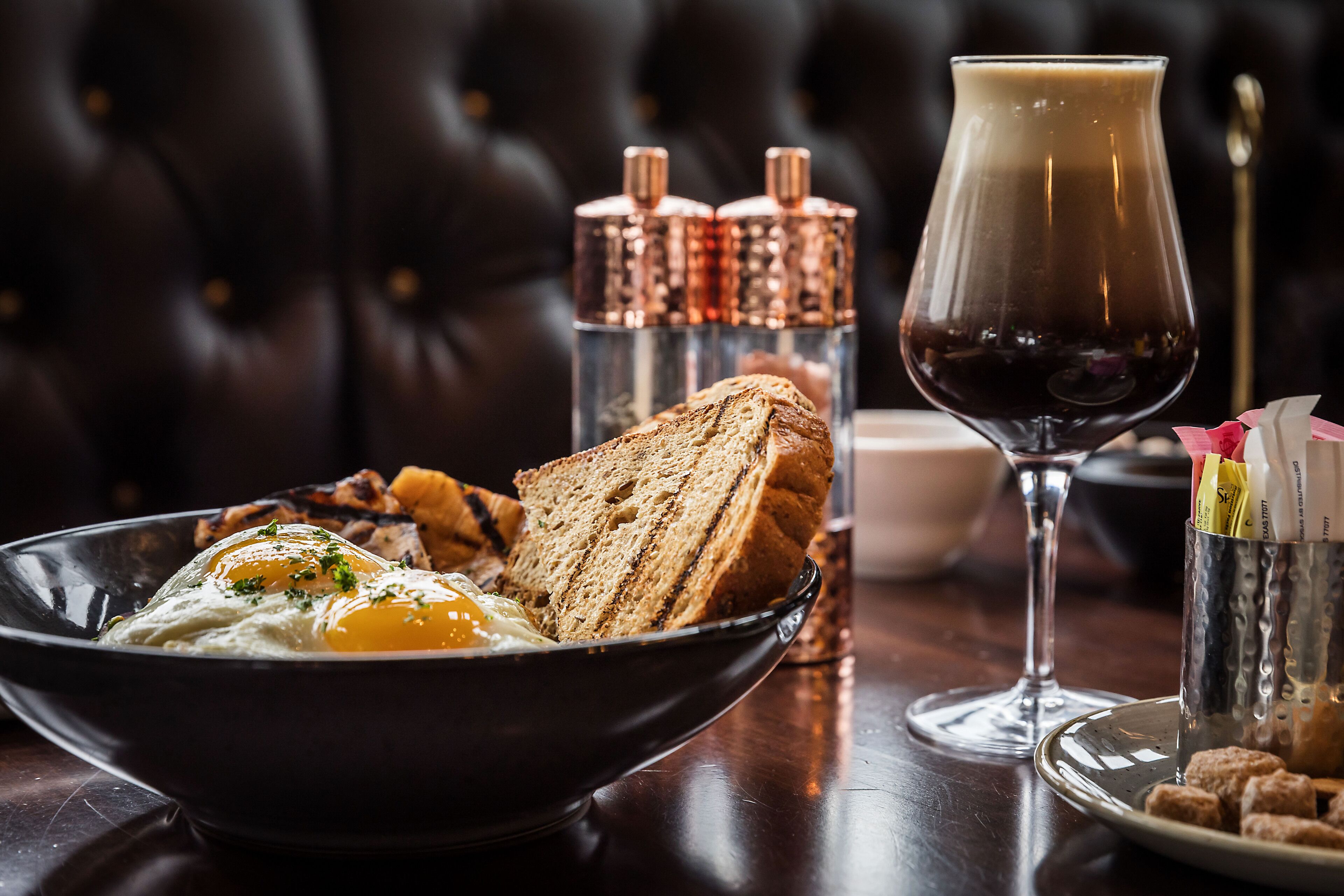 A breakfast setting with a bowl of eggs, toast, and a glass of coffee on a wooden table.