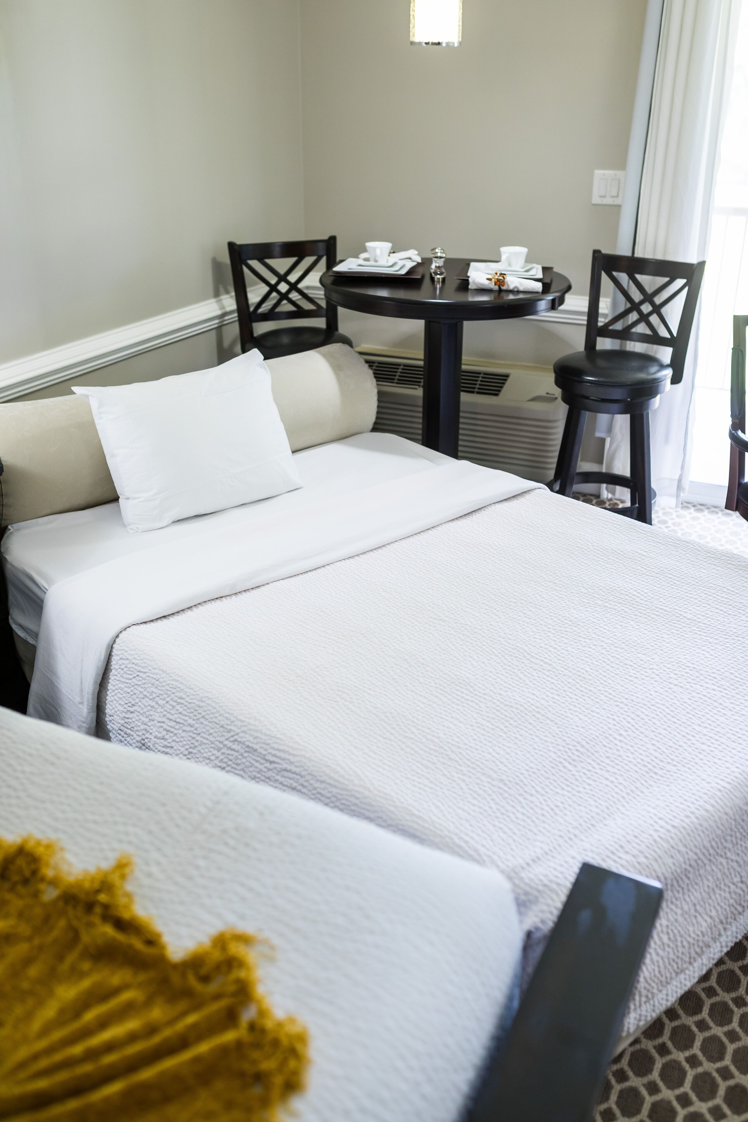 Une chambre d’hôtel avec deux lits, une petite table avec une chaise et une fenêtre avec des rideaux.