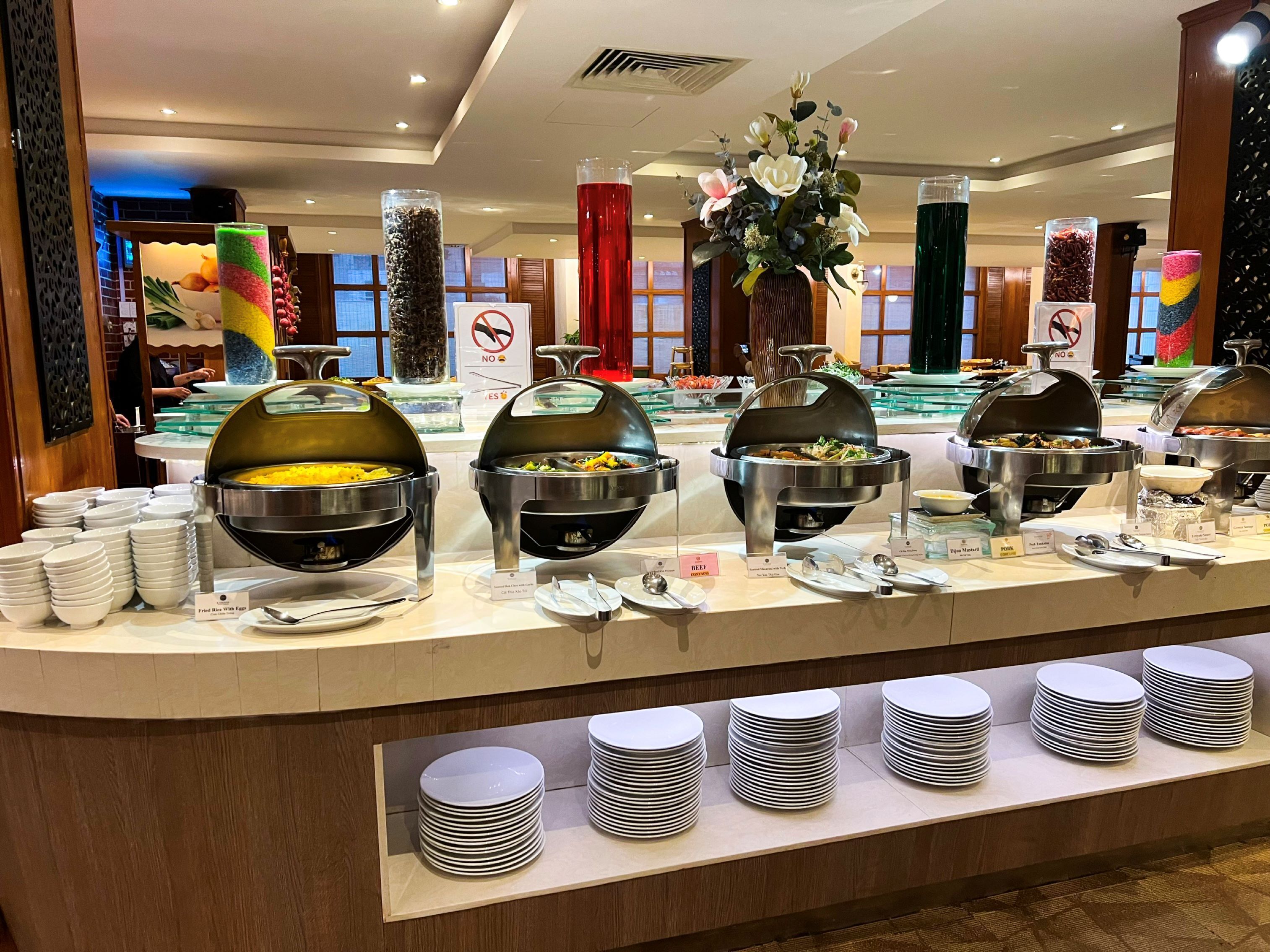 Montaje de bufé con diversas estaciones de comida, incluyendo una estación de carne de res y una de cerdo, con platos y utensilios para servir dispuestos para los huéspedes.