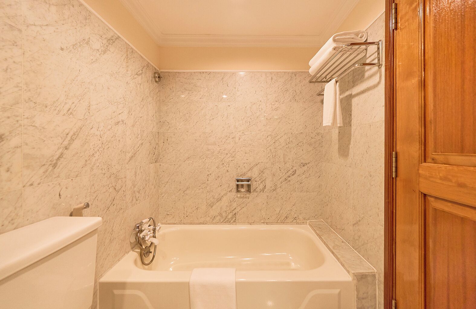 A bathroom with a marble wall, a bathtub, a wooden door, and a towel rack.